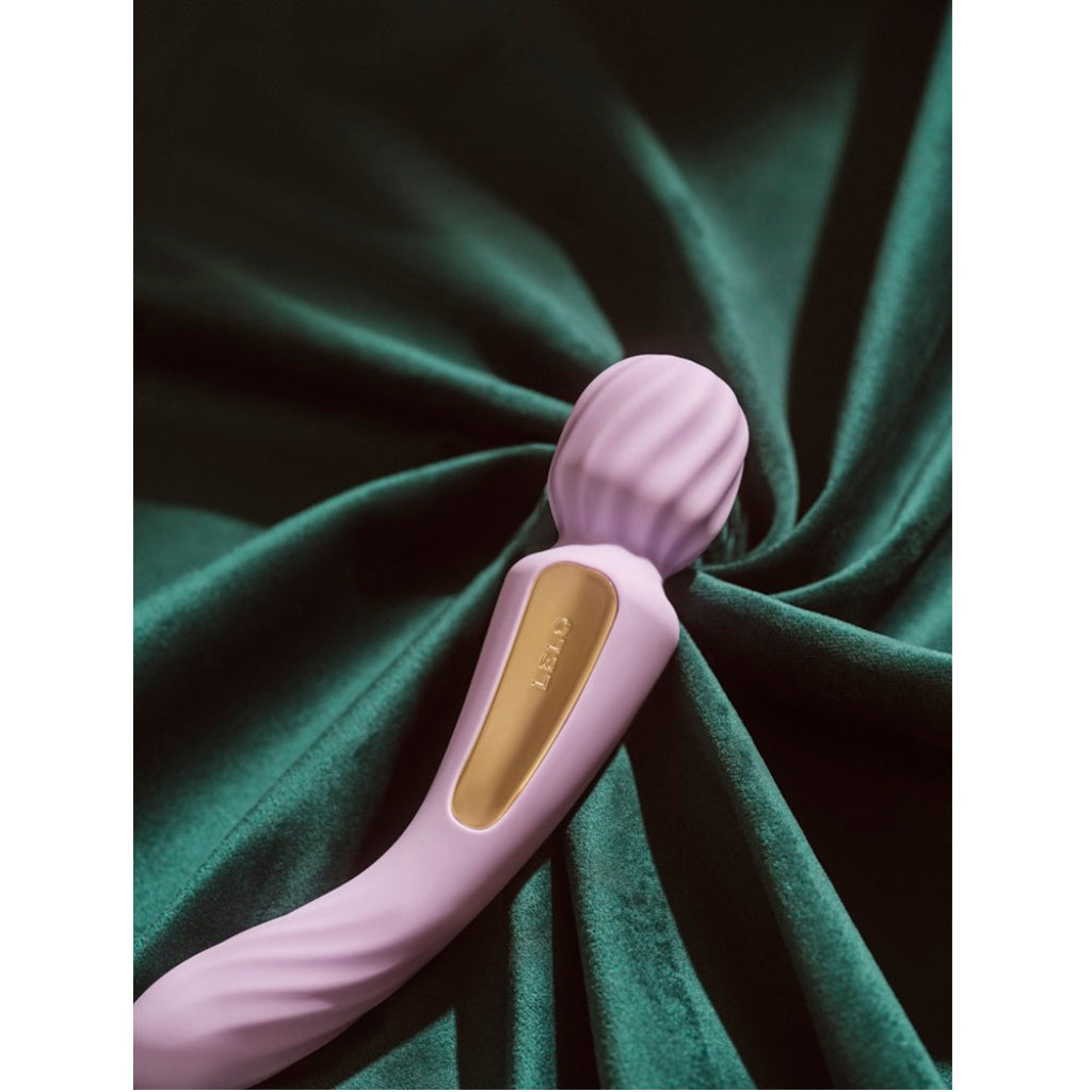 Pink handheld massager with gold logo on green fabric